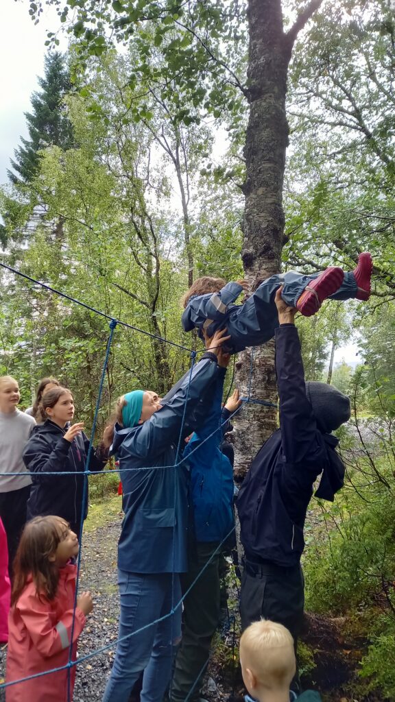 voksne løfter et barn over en hindring i skogen