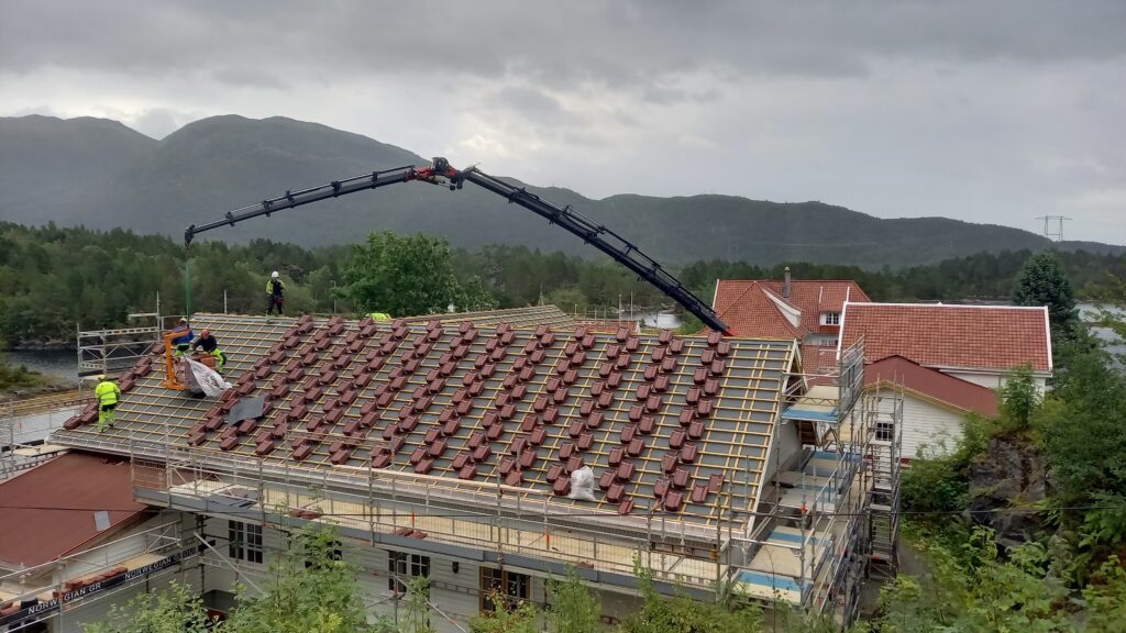 heisekran og takstein plassert på taket på en bygning med arbeidere